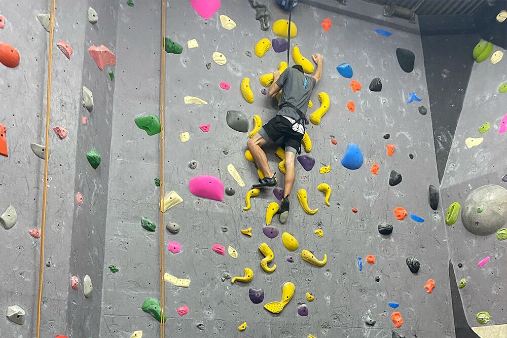 Climber scaling an indoor rock climbing wall, showcasing determination and strength